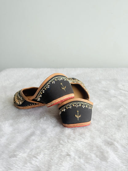 Noor black and gold juttis showing decorative detailing