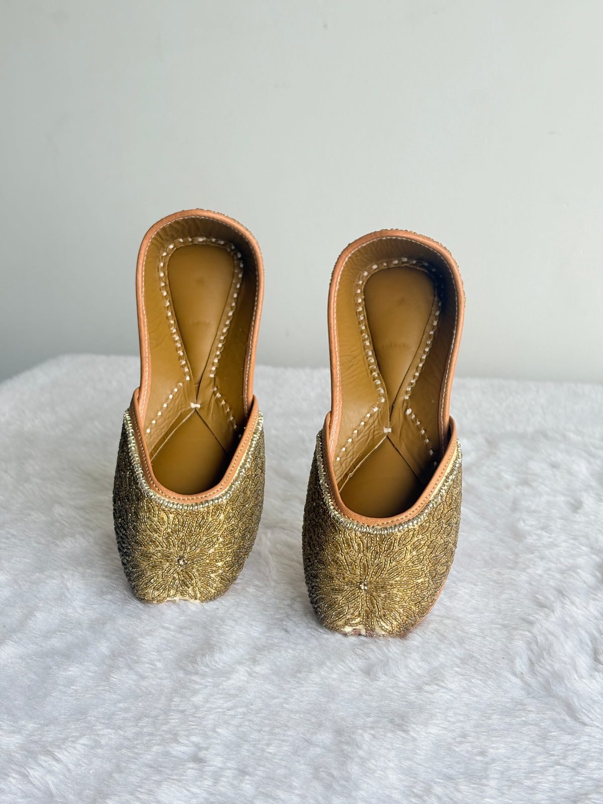 Aurelia Gold Juttis with gold-toned floral detailing, front angled view